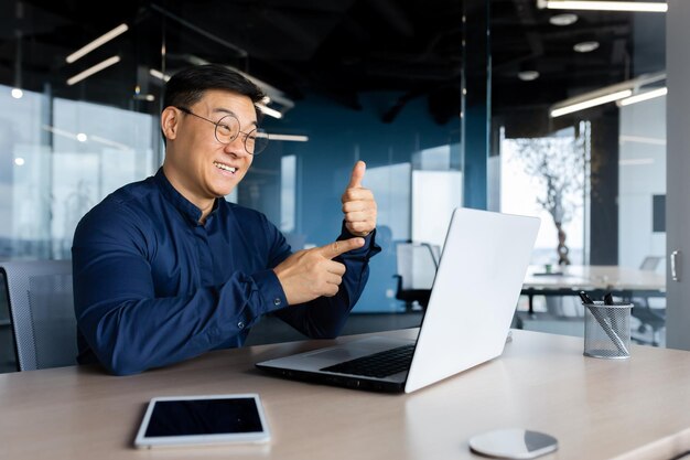 Video call happy asian talking remotely with colleagues businessman inside office with laptop on