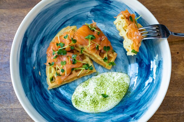 Viennese waffle with salmon and white sauce on a blue plate is eaten with a knife and fork. serving breakfast in a cafe and restaurant. serving the table and serving dishes for the banquet.