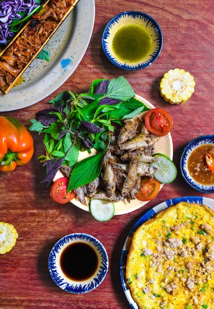 Vietnamese cuisine set made of braised deer in bamboo, fried fish, omelette with sauces on wooden ta