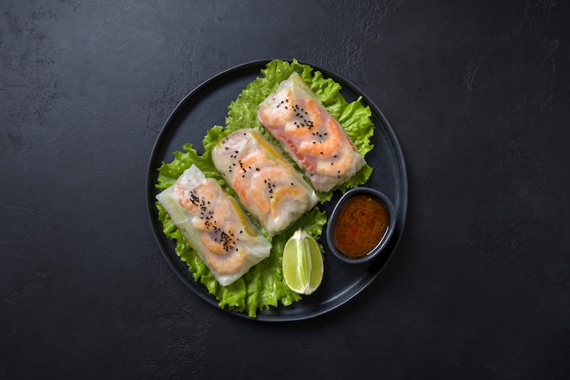 Vietnamese food spring rolls with vegetables, shrimps in rice paper on black. View from above. Asian cuisine.