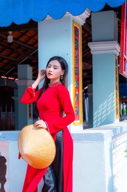 Photo vietnamese girl with ao dai dress standing in traditional house of vietnam text in photo mean best wishes to family happiness prosperity health tet holiday and new year