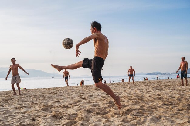 Photo vietnamese man kicks a ball playing beach soccer on beach by the sea in summer nha trang vietnam july 31 2024