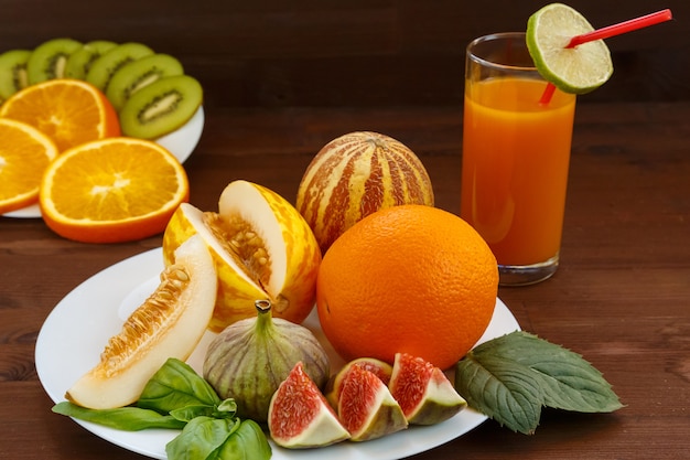 Vietnamese melon, lime, figs, orange, kiwi are on a white plate with a dull background