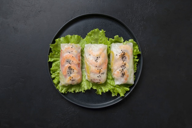 Vietnamese spring rolls with shrimp in center of black table. Asian cuisine.