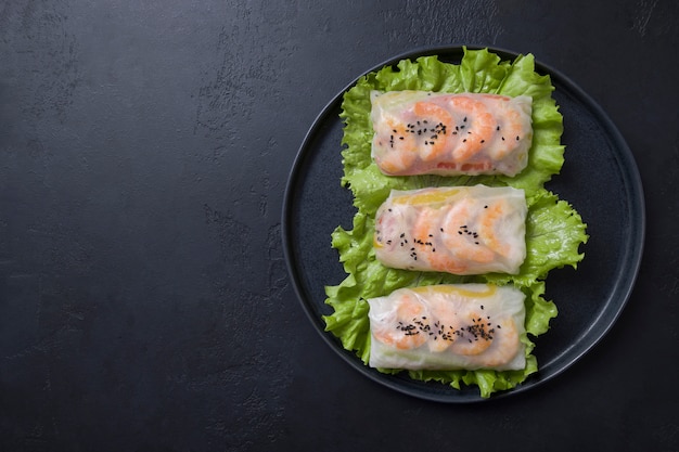 Vietnamese spring rolls with vegetables, prawns in rice paper on black. Asian cuisine.