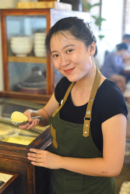 Vietnamese waitress showing a scoop of homemade mango ice cream in cafe