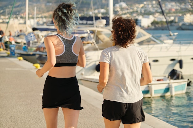 View of the back of mother and daughter running at seaside promenade