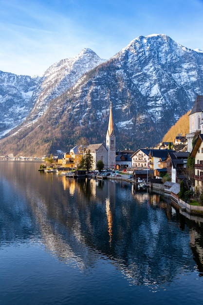 VIew of beautiful Hallstatt lake and famous church during morning sunrise in early spring with mountain ranges covered in some snow