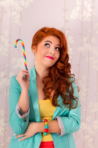 View of a beautiful redhead girl with a candy stick wearing colorful clothing.