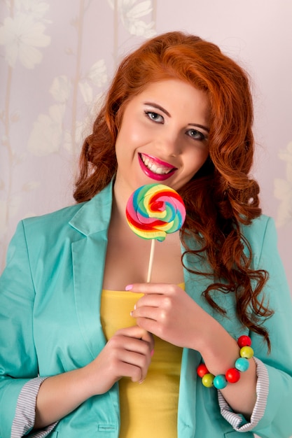 View of a beautiful redhead girl with a lollipop candy wearing colorful clothing.