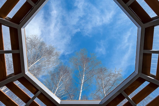 View of blue sky through wooden frame lattice Window on roof of alcove view of sky and treetops Calm and serenity on clear spring day