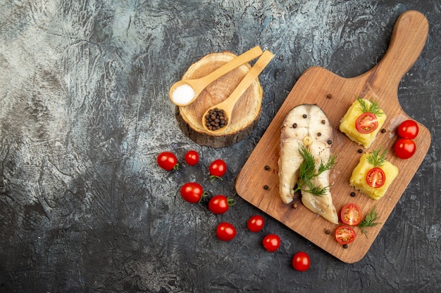 Above view of boiled fish buckwheat meal served with tomatoes green cheese on wooden cutting board spices on ice surface