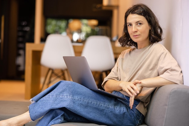 View of cheerful woman sitting at couch in home look at camera