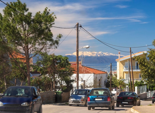 View of city street with vehicles sea and Parnassus mountains on the horizon in the snow in Greece