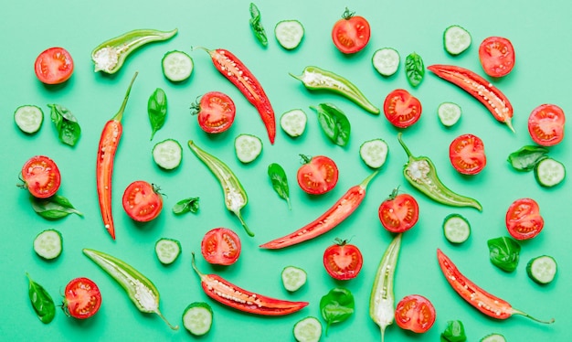 Above view at cutted Chili pepper and basil with tomatoes and cucumbers on green background