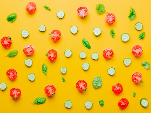 Above view at cutted tomatoes, cucumbers and basil on yellow background