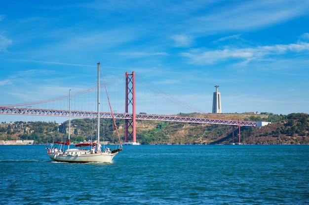 View of de abril bridge over tagus river christ the king monument and a yacht boat lisbon portugal