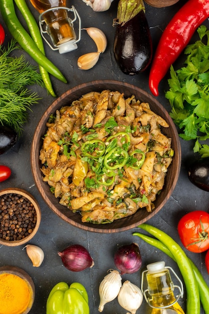 Above view of delicious eggplant meal fresh vegetables spices fallen oil bottle green bundle on dark color background