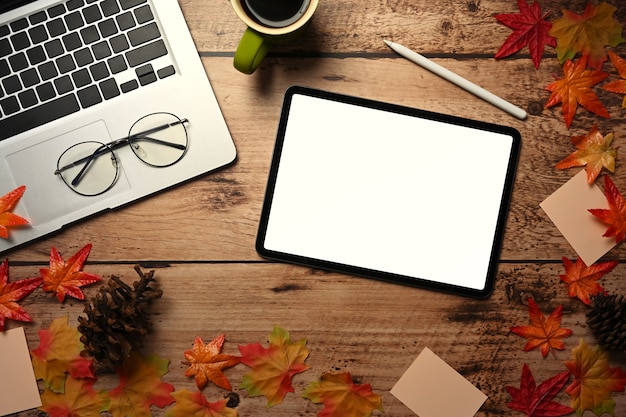 Above view digital tablet, laptop computer, coffee cup and autumn maple leaves on wooden table.