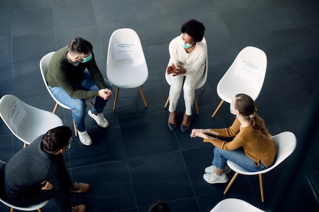 Above view of f members of group therapy wearing face masks while talking on a session