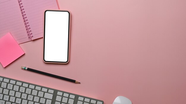 Above view of female workspace with smart phone, keyboard, notebook and copy space on pink table.