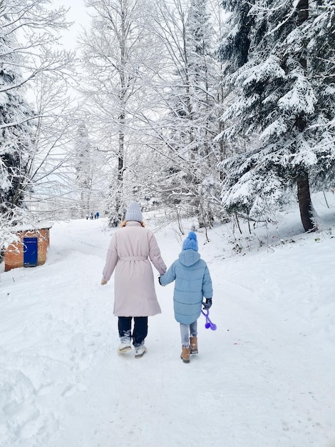 View from back mother and daughter walk through a snowcovered forest or park