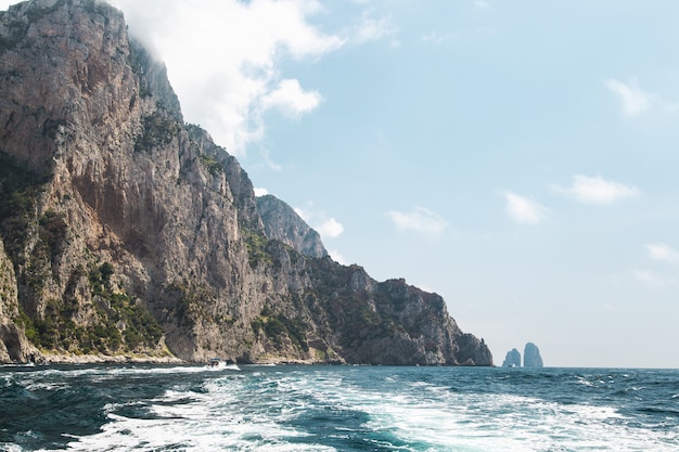 View from the boat on Capri island coast and faraglioni oceanic rock formation.