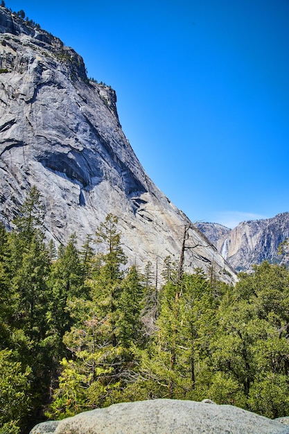 View from boulder of yosemite valley filled with pine trees and waterfall in distance