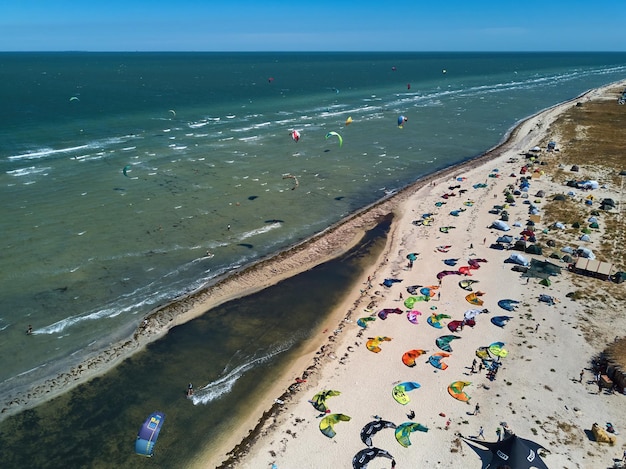 View from above of bright colorful kites lying parked on beach on windy day at kitesurfing spot A lot of parachutes for kiteboarding lie on shore line Extreme water sports Aerial drone photo