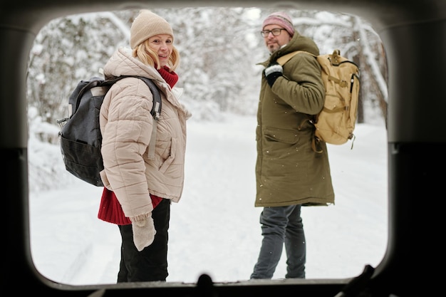 View from car trunk of mature couple of backpackers standing in the forest