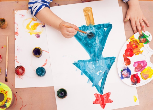 View from above. child draws a brush and paints on white paper