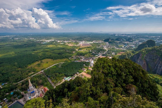 View from the cliff to the Tiger Cave temple and green fields. Small houses in the distance. Clouds in the blue sky.