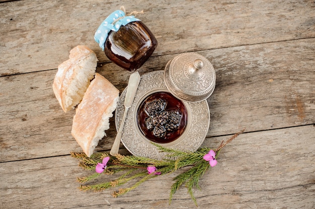 View from above on the cones jam in the silver plate with a cap, tree branch and bread near it on the wooden table