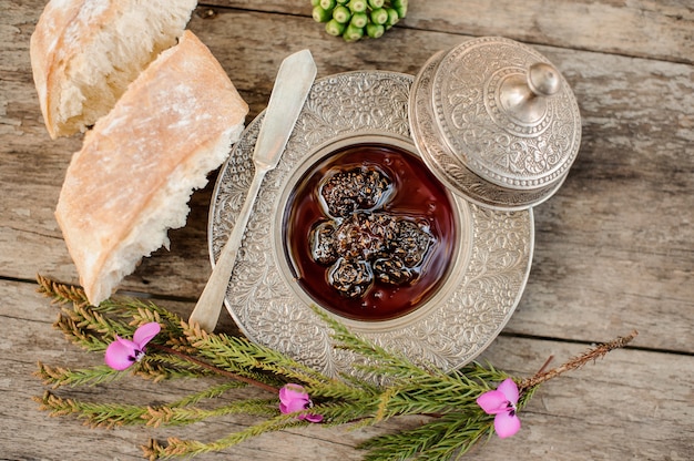 View from above on the delicious cones jam in the silver plate with a cap, tree branch and bread near it on the wooden table