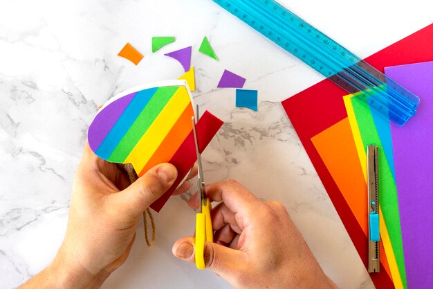 View from above of the hand of a person cutting out with a scissors colored stripes to line a heart representing the LGBT movement