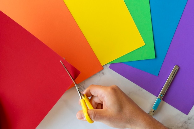 View from above of Hand of person cutting out with a scissors several colorful leaves