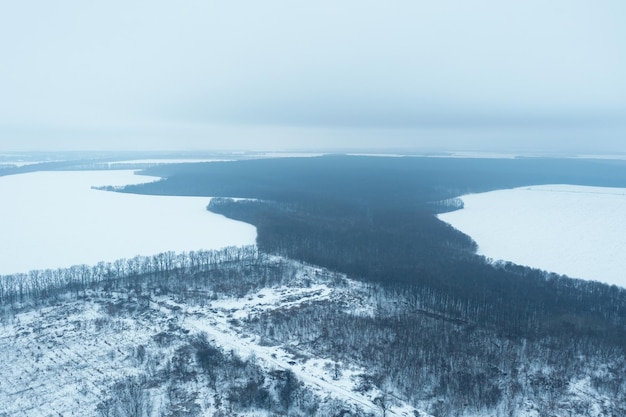 View from a height of a winter landscape with a snowy field forest and fog