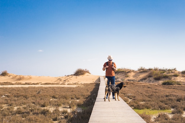 View from behind of a man walking with his dog on a road leading through beautiful landscape.