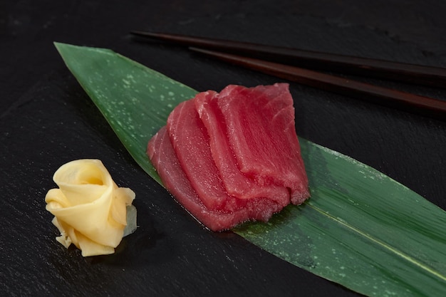 View from above of pieces of tuna on bamboo leaf and ginger with wasabi to be cut and prepare sushi