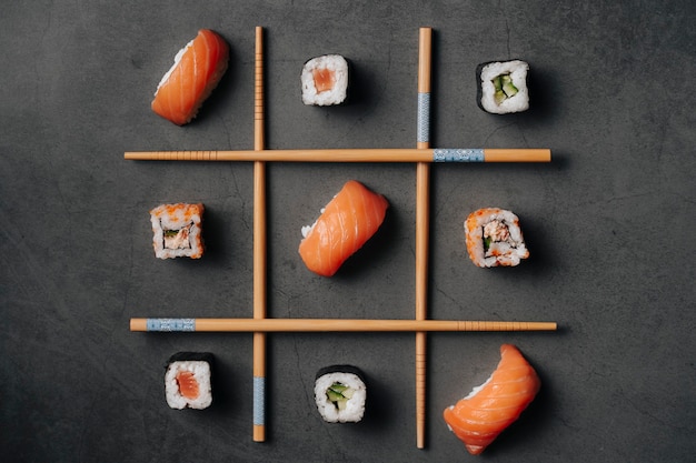 View from above of some Japanese sushi rolls and some pieces of salmon with rice making a very original shape and placed like the three in grates with chopsticks.