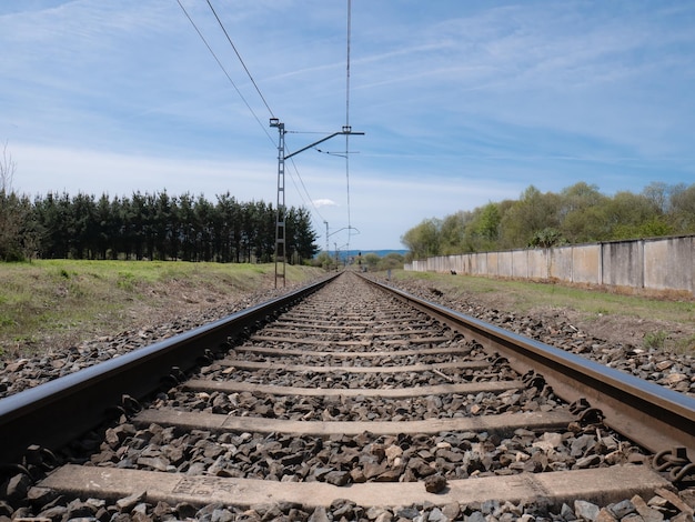 View from the train tracks towards an infinite straight between sleepers and the ballast under the wires of the catenary