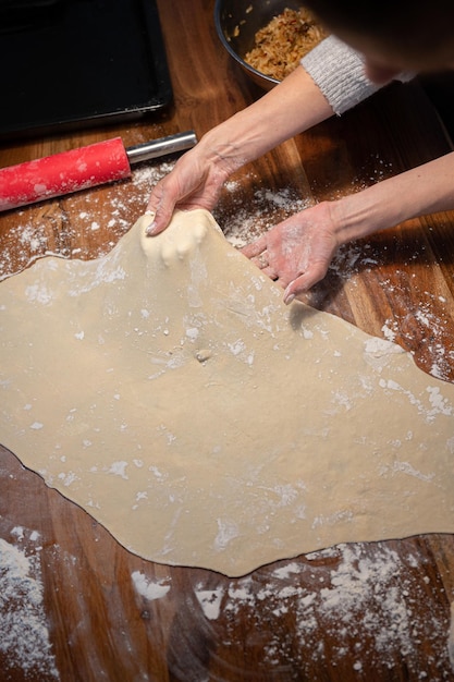 View from above of a woman pulling and stretching homemade pastry dough for strudel or pie