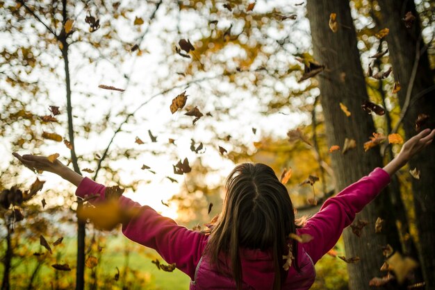 View from behind of a young woman standing in autumn woods with her arms outstretched