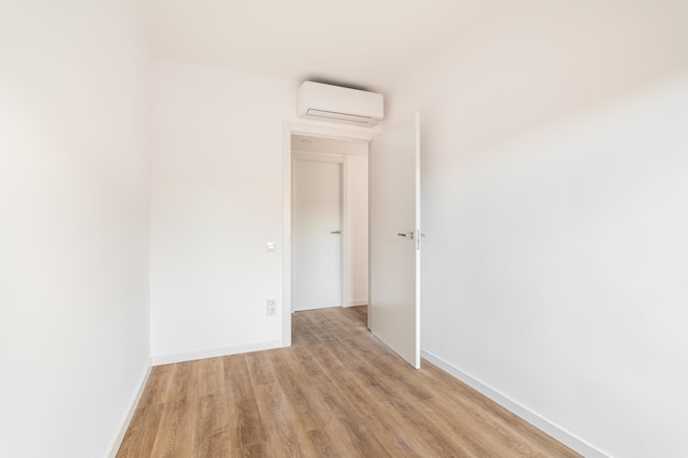 View of the front door to a small white airconditioned room with wooden floor in a hotel concept of