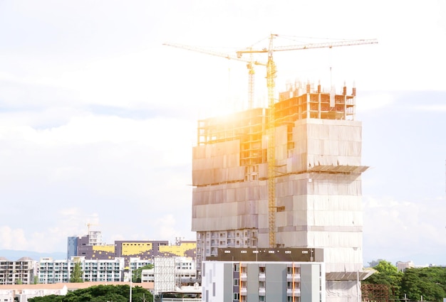 View of hoisting cranes working building construction and city scape with sun flare background