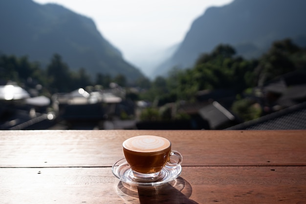 View of hot milk tea latte art on wooden table with relax scenery at Pha Hee Village ,Chiang rai , Thailand