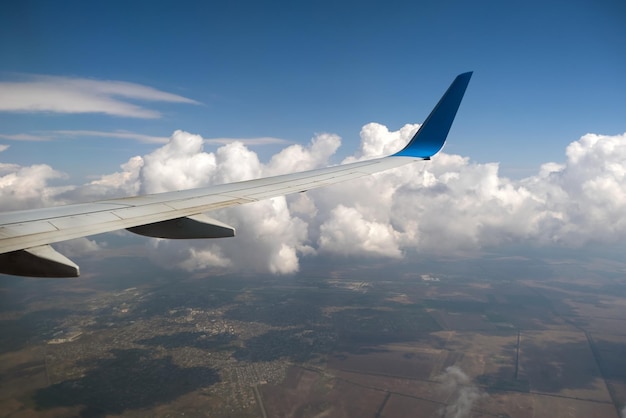 View of jet airplane wing from inside flying over white puffy clouds in blue sky. Travel and air transportation concept.