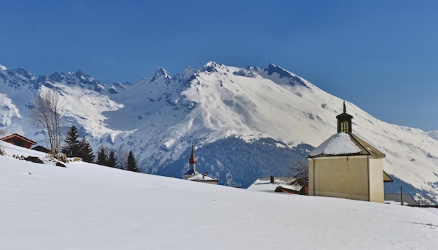 View on a little chapel in alpine snowcapped mountain in savoie and under blue sky