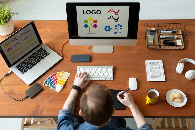 Photo above view of logo designer sitting at desk and editing icon design using drawing pad