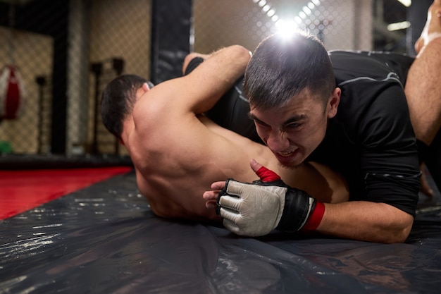 View of low angle of two professional fighters battling in gym. Strong boxers with perfect body fighting, try to win the fight, aggressive strong men engaged in sport MMA